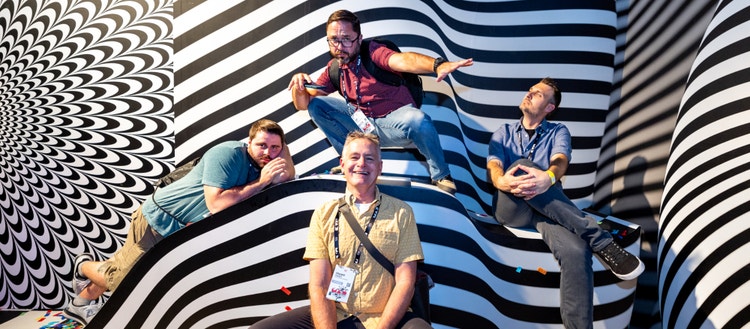 4 men sitting against a black and white striped wall