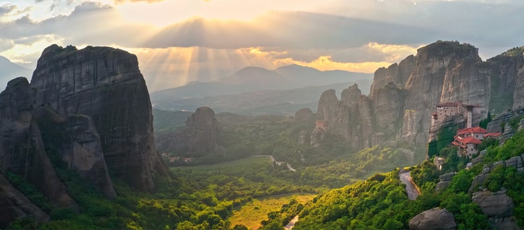 Meteora Greece. Sunset sun rays through sky clouds in mountain valley.