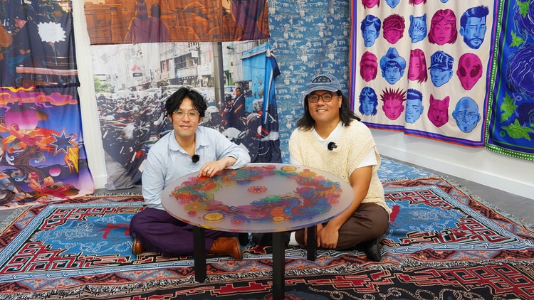 Chris and Andrew Yee sitting surrounded by colourful tapestries