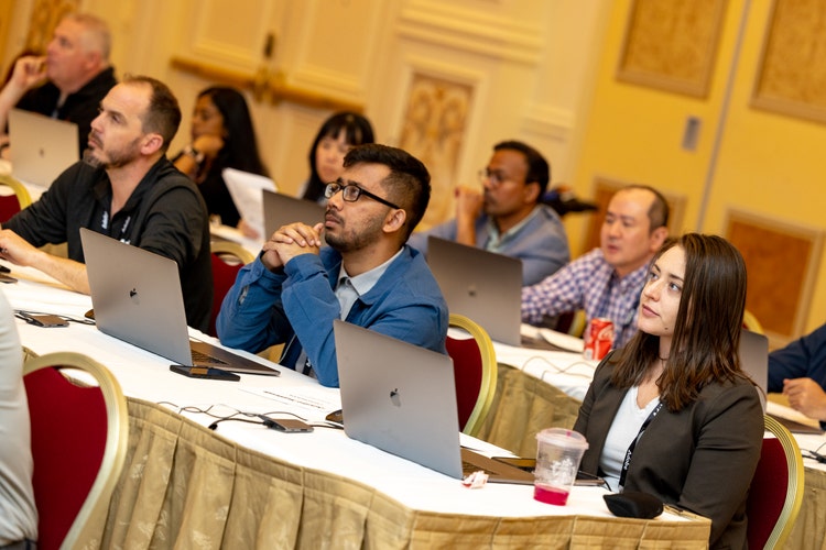 Image of a goup of people sitting at tables with laptops open.