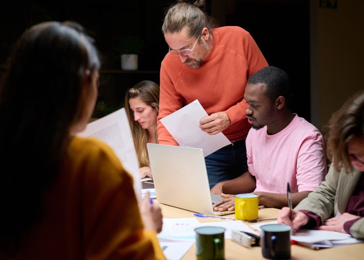 Image of a man standing over people working at a desk.