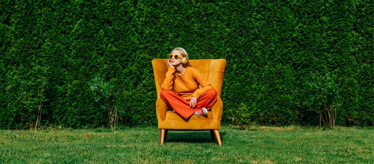 Blond woman sitting on armchair in garden.