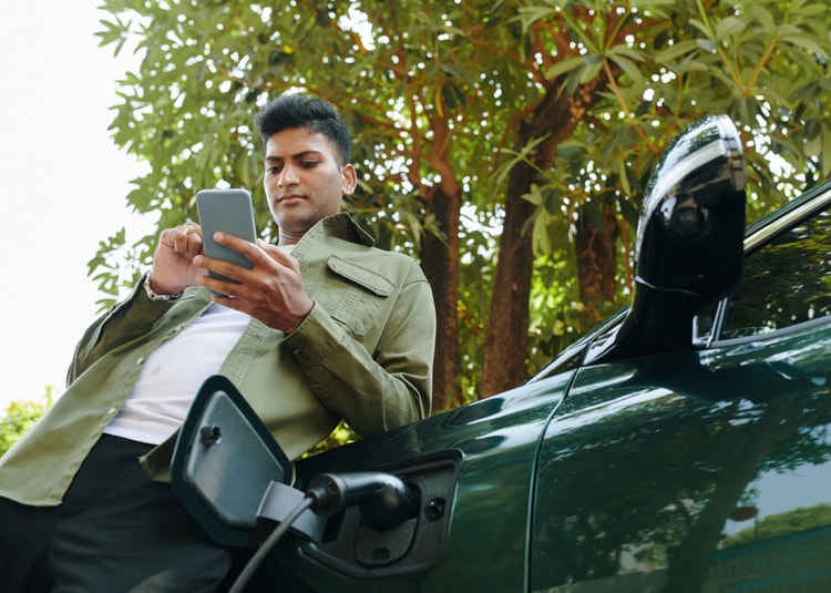 Electric car owner checking notification on smartphone when waiting for his vehicle to charge.