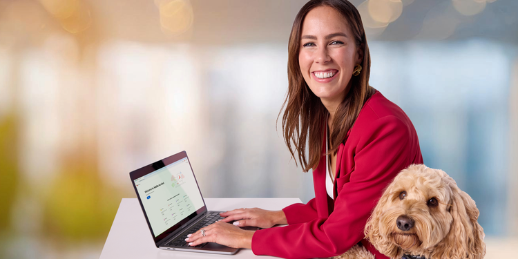 Sarah Bolitho (Caucasian, female), sitting in front of her laptop with her pet dog, smiling at camera.