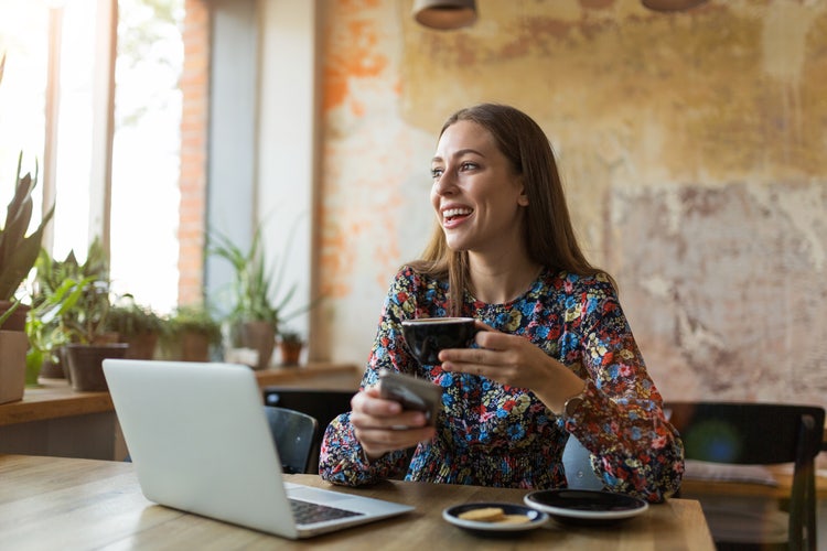 Image of smiling woman holding a tea cup by her laptop.