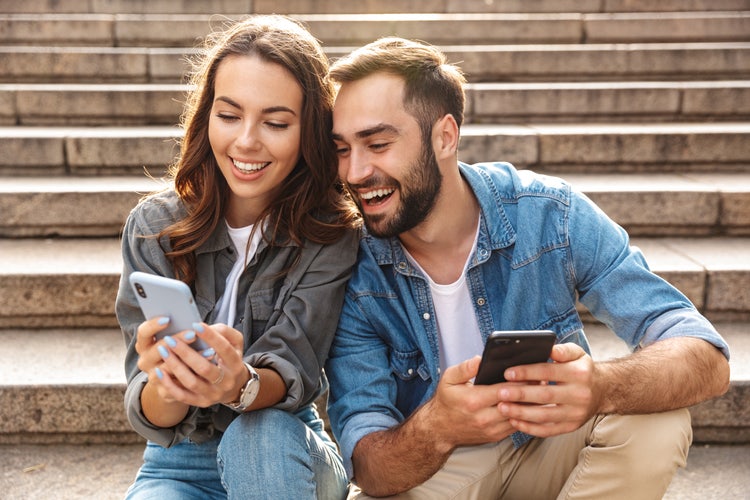 Image of two people smiling while looking at their phones.