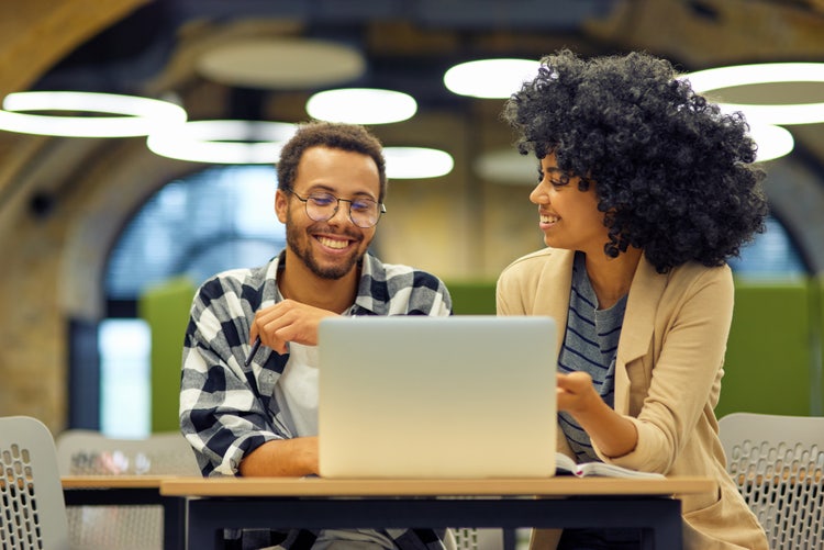 Image or two people smiling while looking at a laptop.