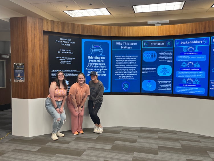 Students in Dr. Wells’ Police and Society class pose in front of their digital presentation created with Adobe Express.