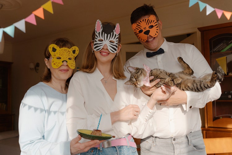 Photograph of three people wearing animal masks with one holding a cat.