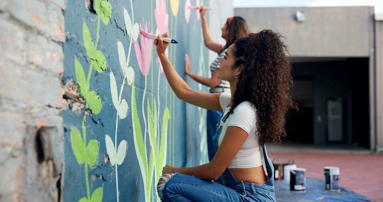 Girl, teamwork or artists painting on wall for mural, drawing flowers
