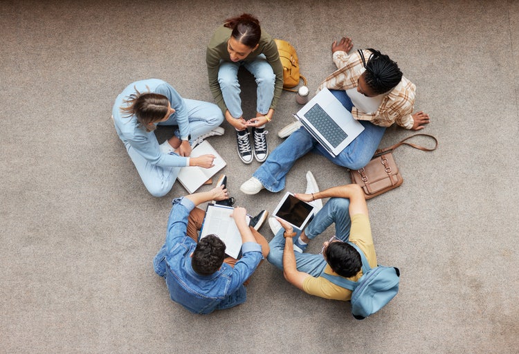 Image of a group of students sitting in a circle on devices.