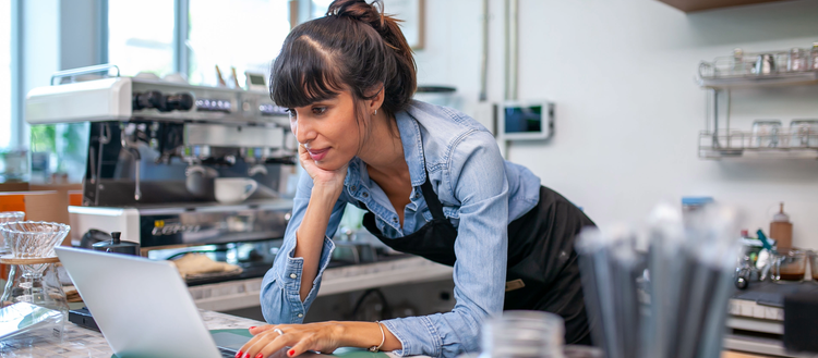 Woman leaning on a countertop using a laptop.
