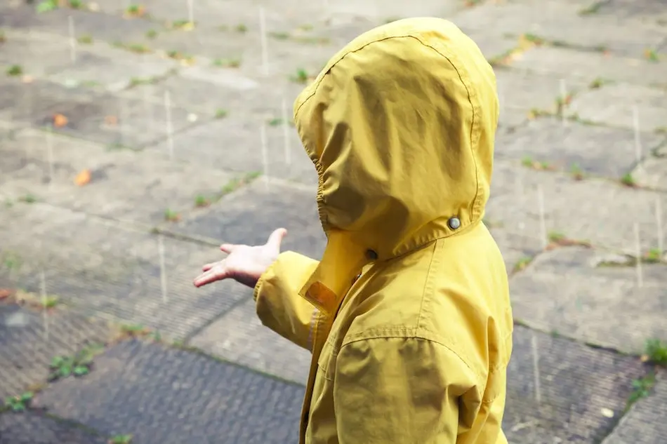 Little child in yellow raincoat playing with raindrops. Vintage stylized tonal correction photo filter effect