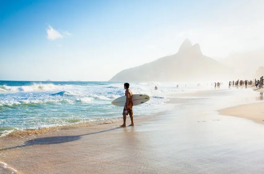 Brazilian surfer walking with surfboard toward Two Brothers Moun
