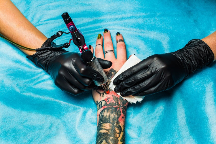Tattooist draws orange paint on clients tattoo