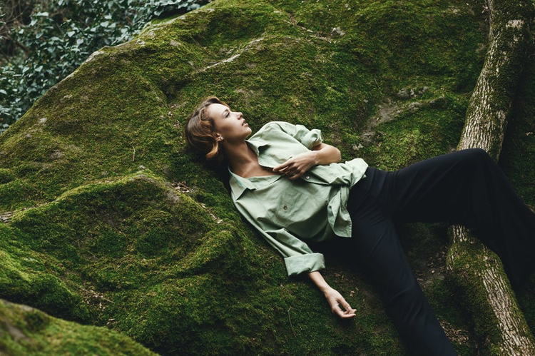 Pretty blonde posing on moss dressed in masculine shirt and stylish trousers.