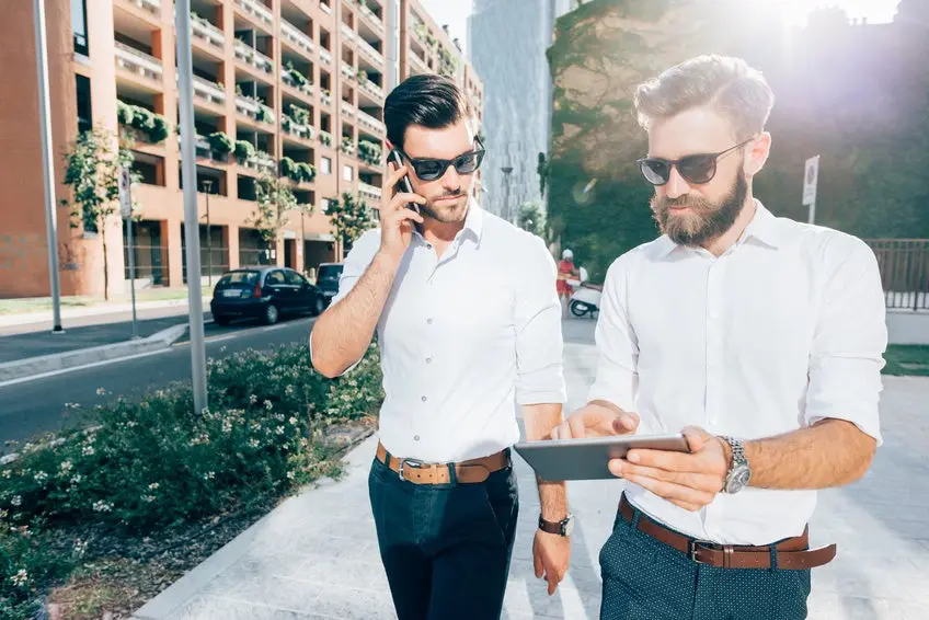 Knee figure of two handsome bearded business man outdoor in the city, one talking smart phone, the other using a tablet hand hold - business, start up, finance, technology concept