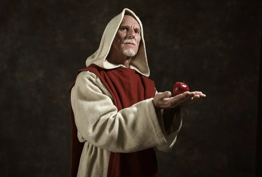 Official portrait of monk holding apple. Studio shot against dark wall.
