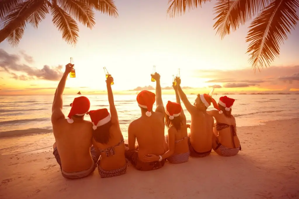 Back view of group people with raised hands holding a bottle of beer on beach, Christmas holiday
