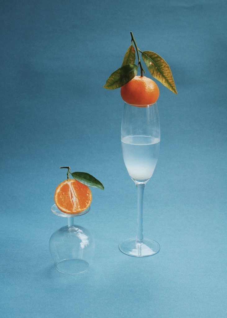 dos copas una volteada y otra con su posicion habitual cada una de llas sosteniendo una mandarina detras una imagen azul 
