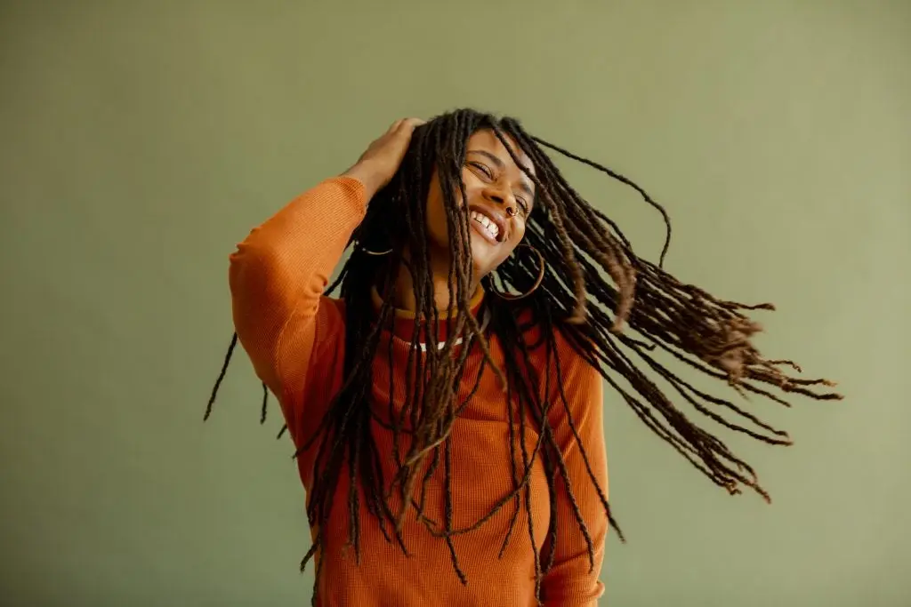 Mujer joven afro feliz moviendo su cabellera con una mano sobre su cabeza Bethany Mollenkof 