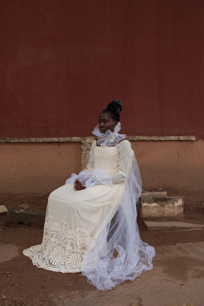 Mujer afro sentada en una silla portando un vestido blanco 