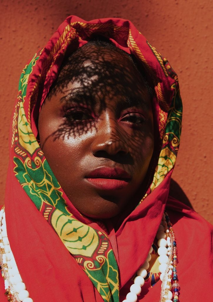 rostro de una mujer joven nigeriana sobre su cabeza una manta de color rojo dorado y verde