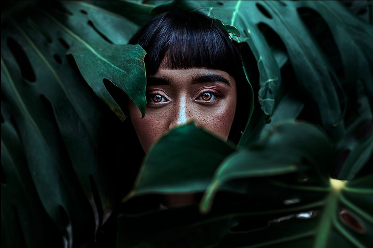 imagen de una joven asiatica detras de unas hojas verdes de un arbol con efecto dramatico