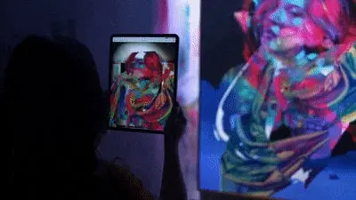 Joven experimentando la realidad aumentada de un cuadro de una mujer con multicolores en su tablet 