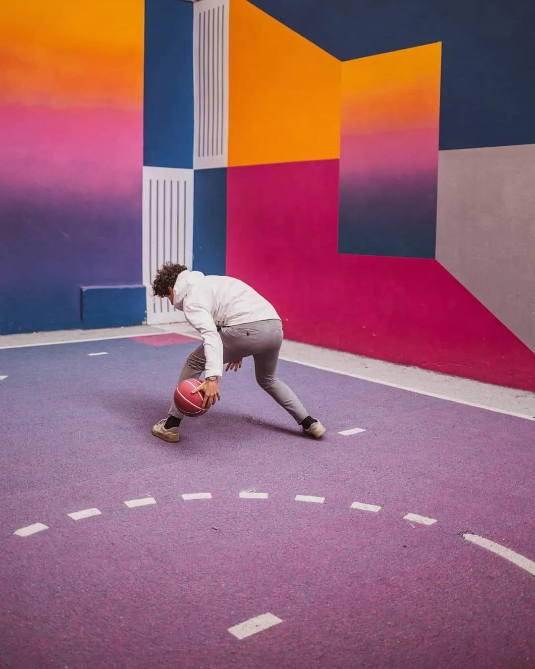 Hombre joven jugando basketball detras una pared pintada multicolor  