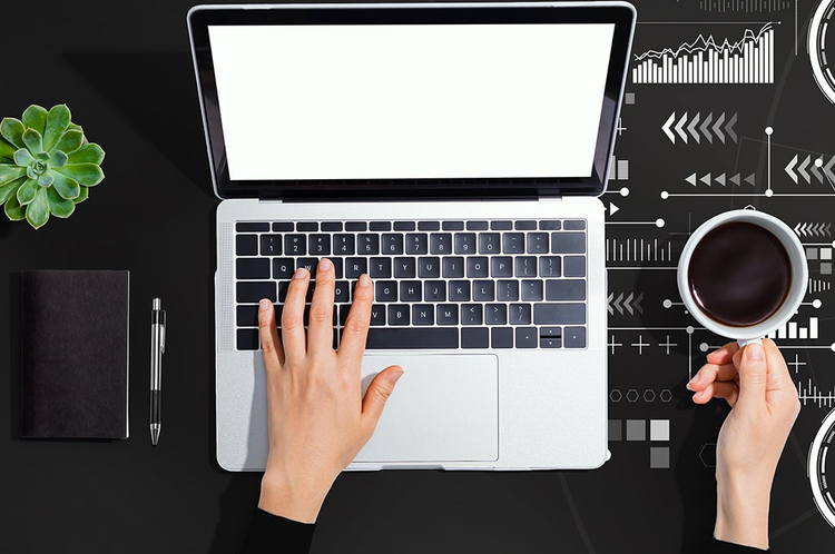 manos de un ejecutivo sobre un computador portatil en su mano derecha una tasa de cafe