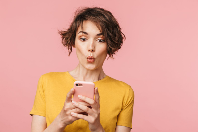 Mujer joven con el cabello corto sorprendida viendo su telefono celular con las nuevas herramientas de adobe photoshop
