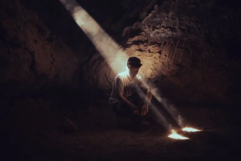 Joven sentado en el piso de una cueva con un viso de luz natural del sol 