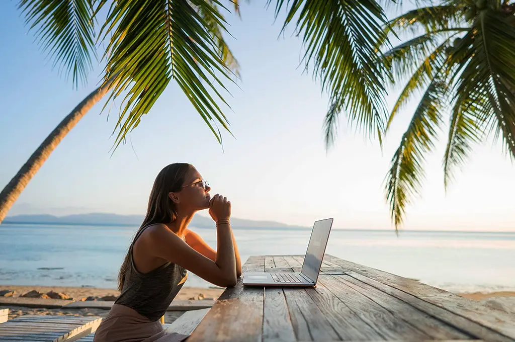 Mujer joven frente a su computador trabajando en la playa, aumentando su capacidad creativa