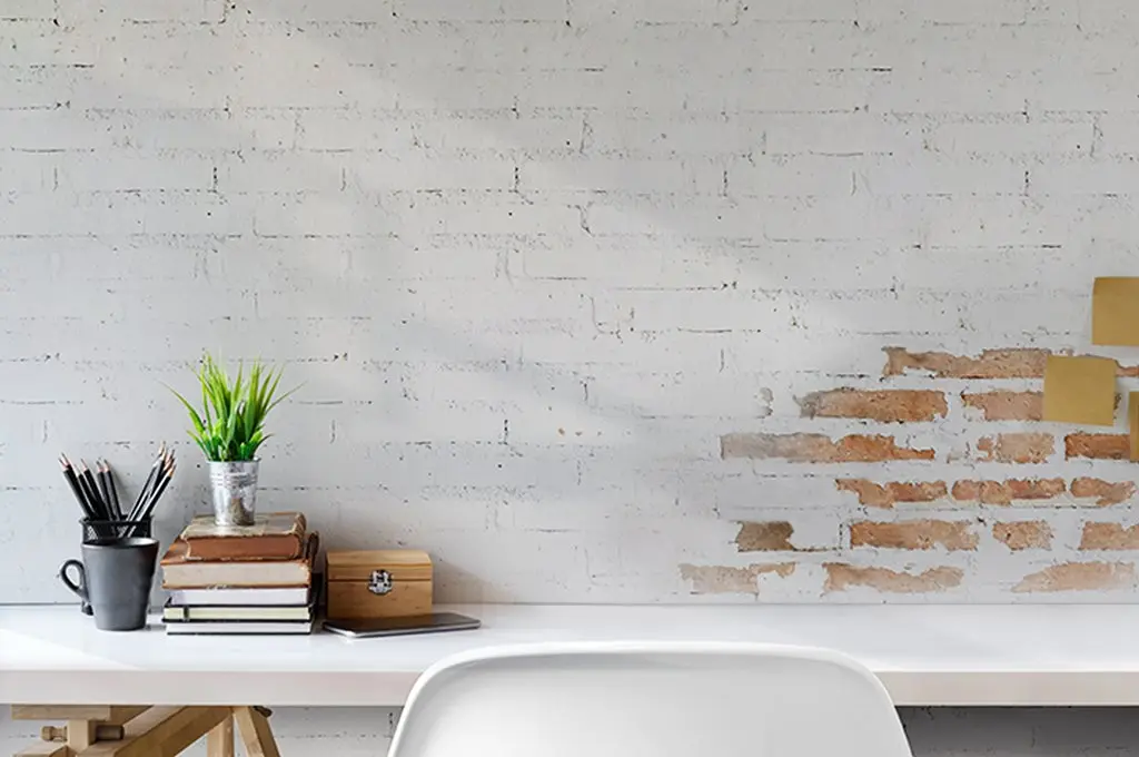 Espacio de trabajo en pared de ladrillo blanca, enfrente una mesa blanca con libros sobre ella