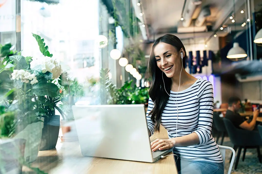Mujer joven sonriendo y trabajando en su computador desde un cafe, cuidadano global, capacidad creativa
