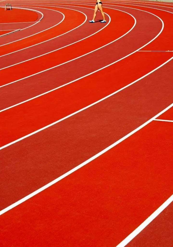 Close-up of red running track with lines and athletic female legs