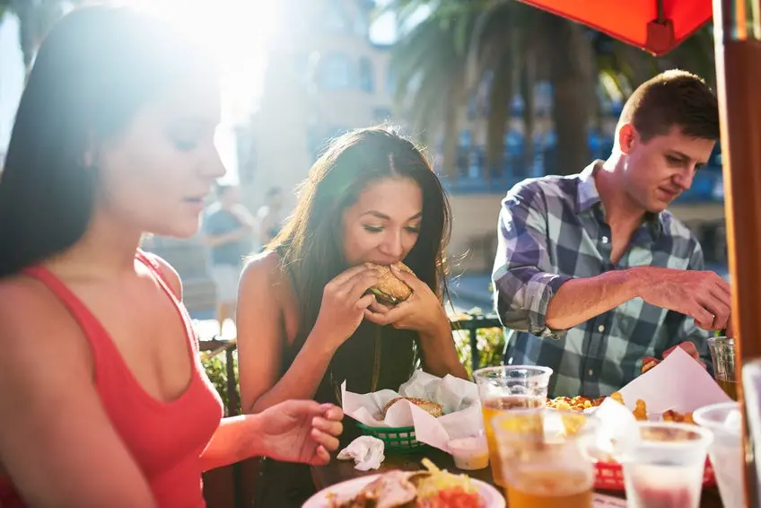 woman eating big burger together with friends at outdoor restaurant