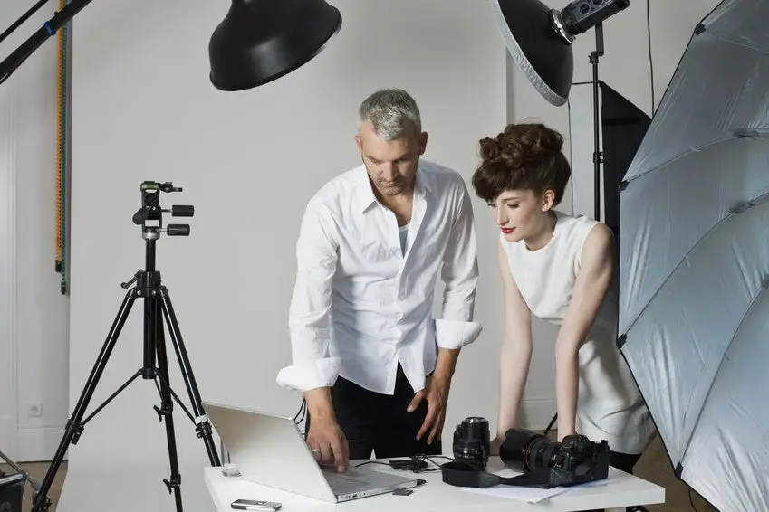 A model and a photographer looking at a laptop computer on the set of a fashion shoot