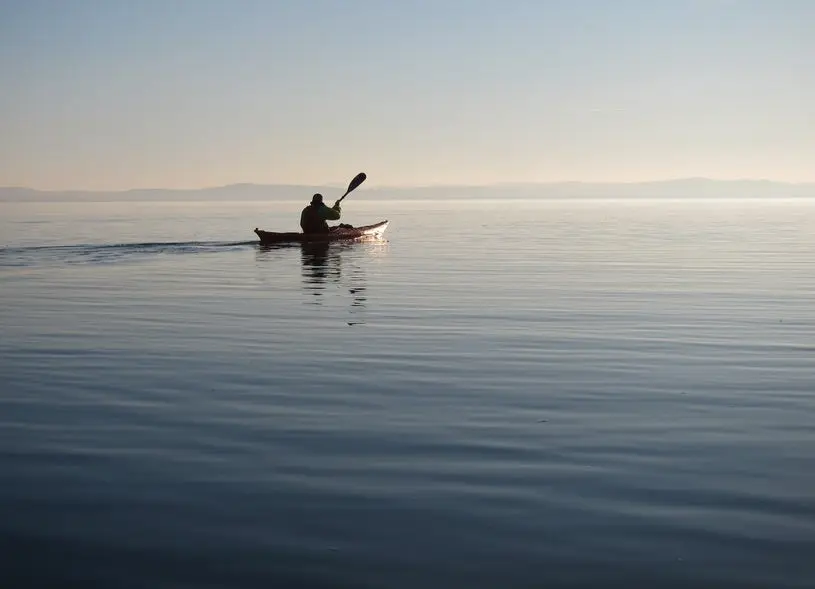 Man on wooden self-made kayak in calm blue lake