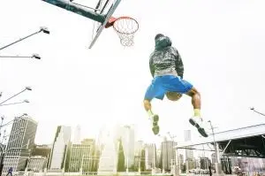 Street basketball player performing an huge rear slam dunk. New york Manhattan buildings background