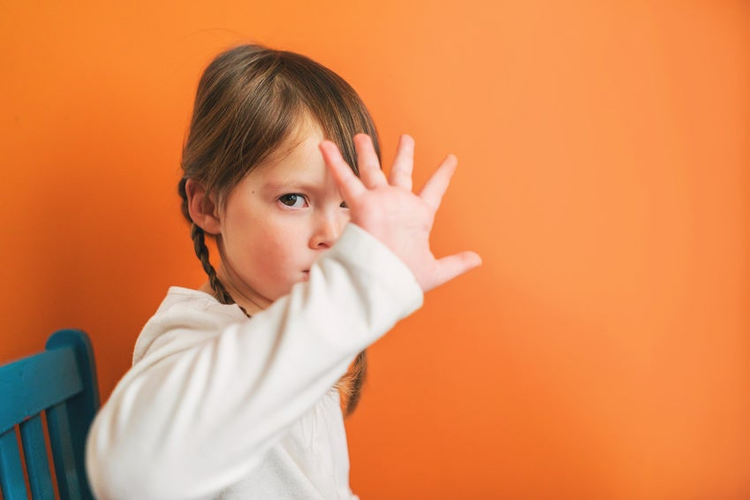 Girl sitting on a chair pouting and holding her hand in front of her face