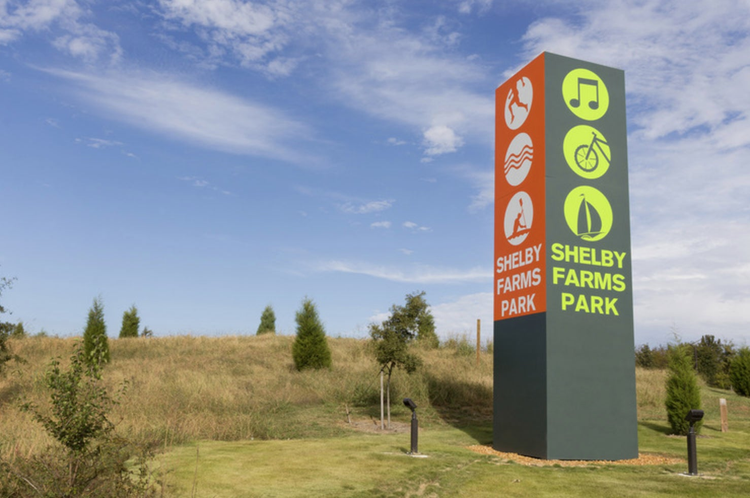 公園の大きくて垂直に立つ直方体の標識には6つのアイコンと大きな「Shelby Farms Park」の文字が描かれている。
