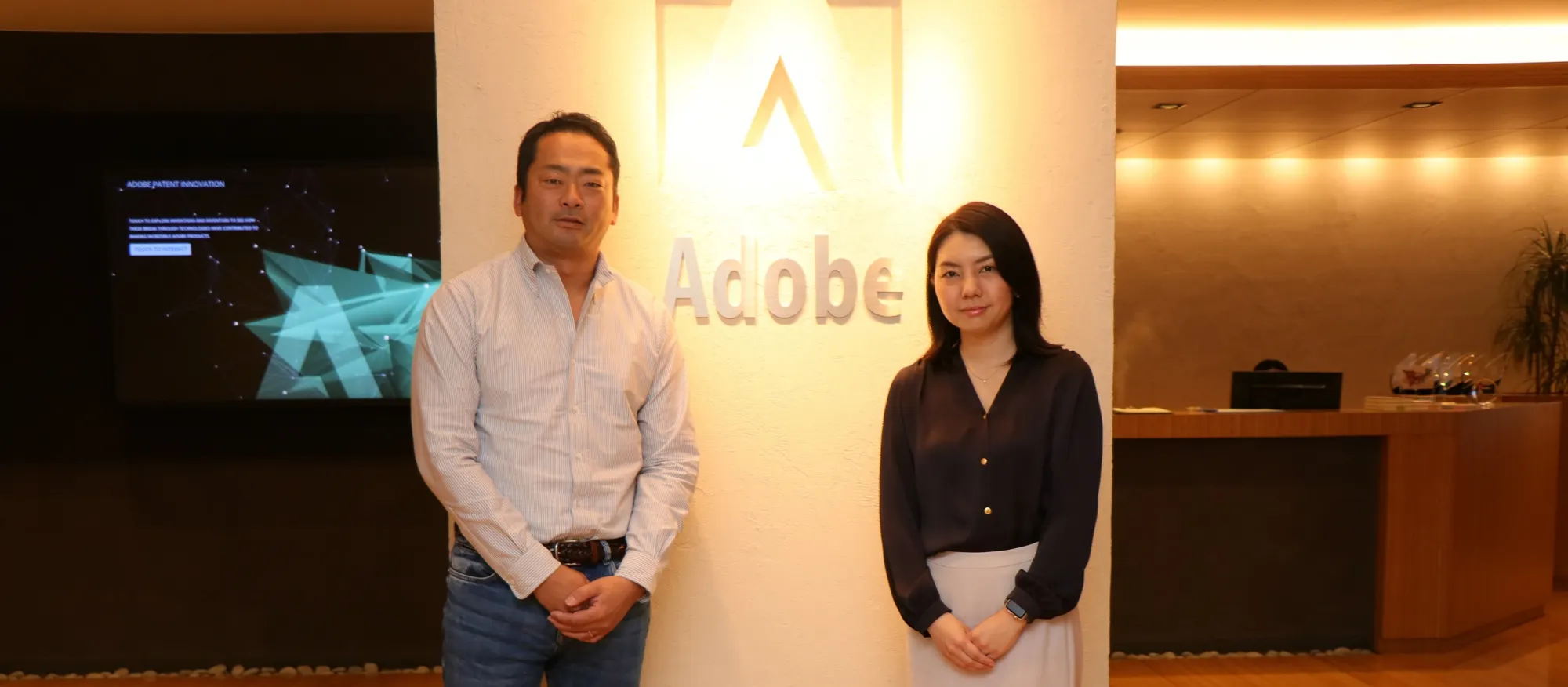 画像:アドビのロゴ前でポーズする社員