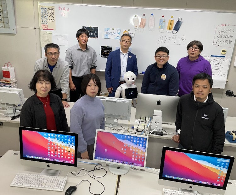 A group of people posing for a photo in front of computers Description automatically generated with medium confidence