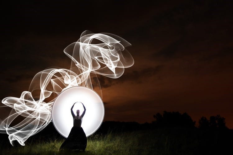 Dark image of woman lit up by swirls of light.