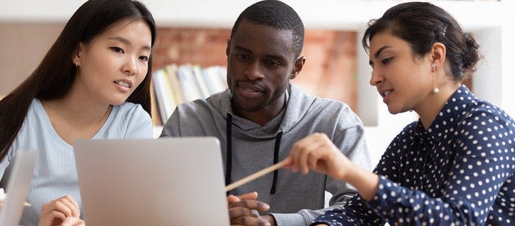 Three university students gathered looking at a laptop.