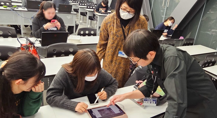 机の上のノートパソコンを見ている人たち 低い精度で自動的に生成された説明