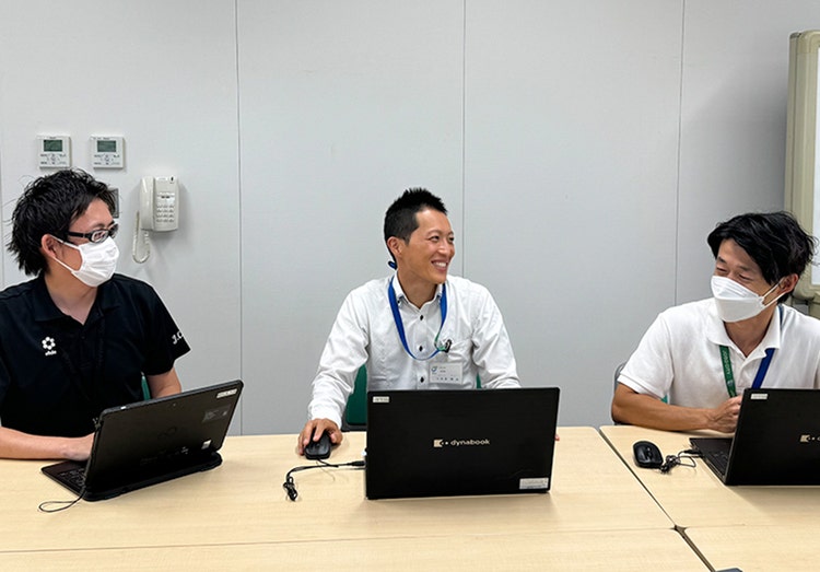 A group of men sitting at a table with laptops Description automatically generated