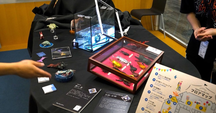 折り紙で制作されたApriori.Art の折り紙アート作品が展示され、来場者が鑑賞している展示ブース
